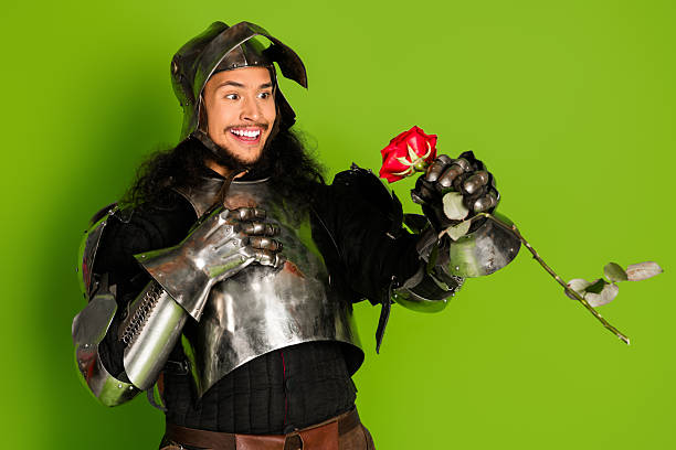 istock Joyful knight in shining armor holding a red rose against a green backdrop 2211232595