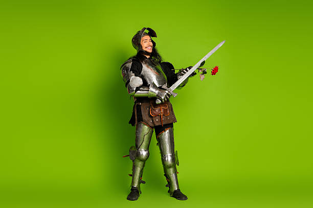 istock Young man dressed as a medieval knight holding sword and rose on a vibrant green backdrop 2211232608