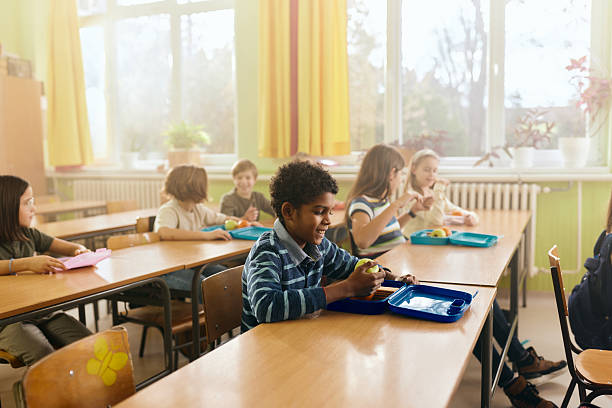 istock Happy black boy having fruit for snack during a break in the classroom. 2211232732