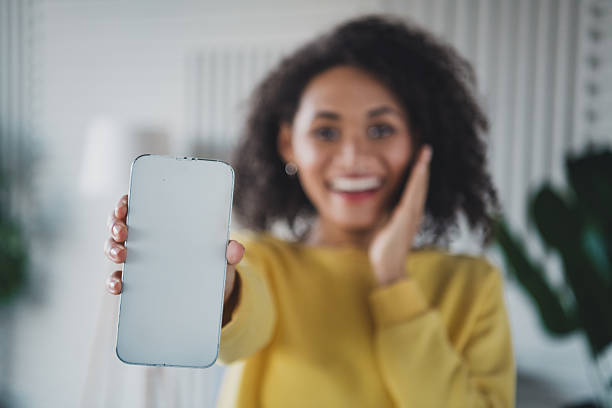 istock Young woman in yellow pullover holding phone with blank screen and smiling indoors 2211234106