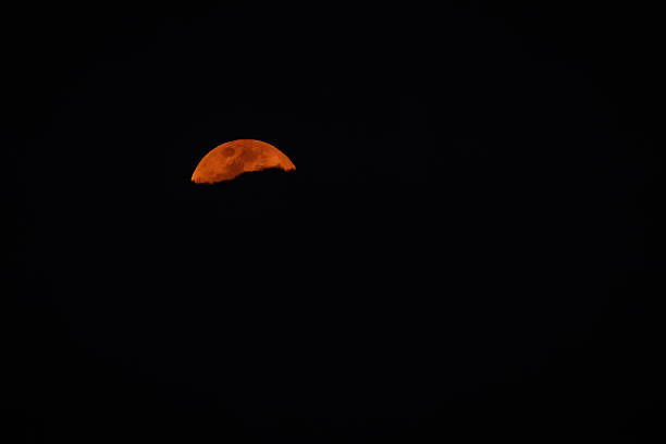 A dramatic partial moon emerges from the darkness of the night sky, casting a warm, mysterious glow over Panyame, Mozambique. This photo was taken in Mozambique.