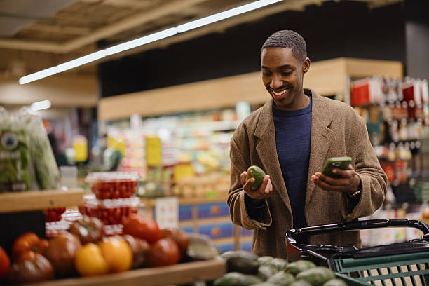 istock Happy black man using smart phone while buying avocado at greengrocer's shop. 2211238665