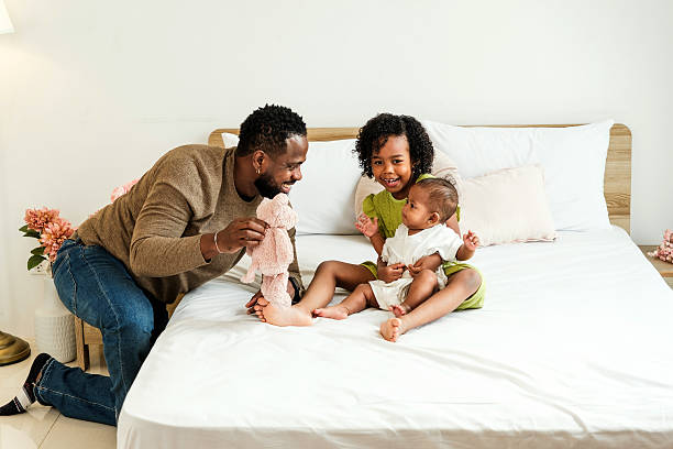 istock Joyful father plays with his daughters on a cozy bed, celebrating love and connection on Father's Day. Warm, authentic moment showing diversity, family bonding, and positive parenting at home. 2211246004