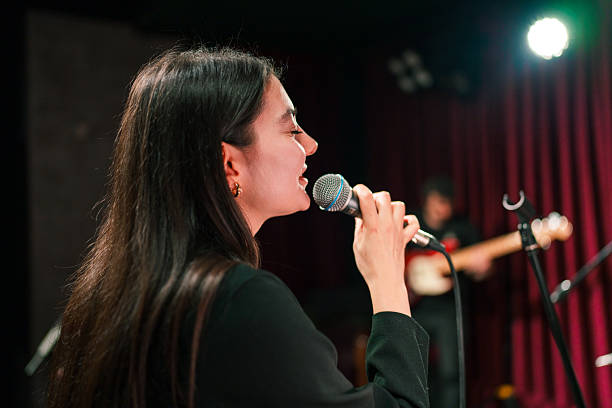 Close-up of women's lips painted with burgundy lipstick and retro microphone. Female singer with disco mic on bokeh light background. Redhead girl starting concert. Copy space for gig posters.
