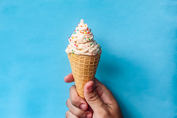 istock hand holding vanilla ice cream cone with sprinkles isolated on blue background 2211249156