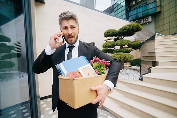 istock Man in suit talks on phone while experiencing job loss outside office 2211250573