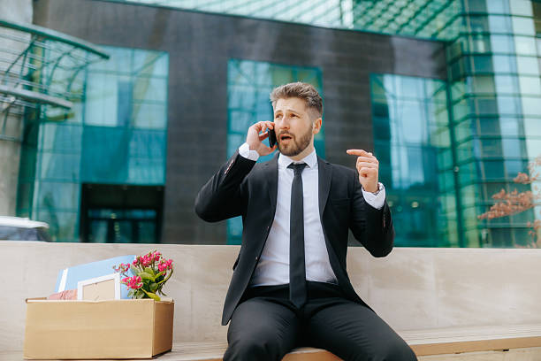 istock Man in suit talks on smartphone while facing job loss outside office building 2211250596