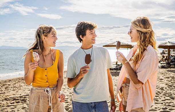 istock Young friends enjoying ice cream and conversation on beach 2211255847