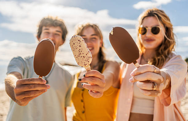 istock Young friends showing ice cream on a sunny beach 2211255878