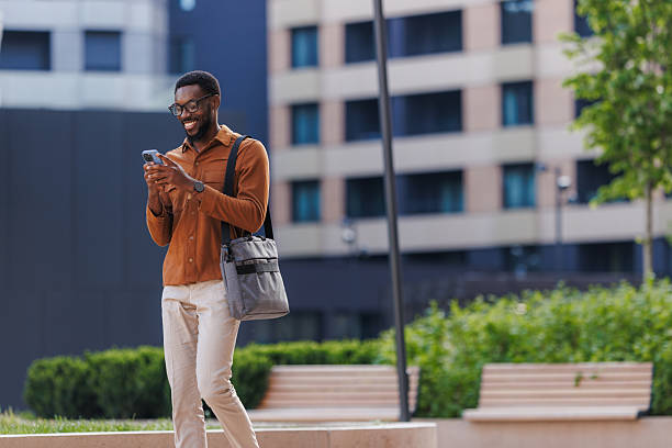 istock Smiling man walking in urban area while using smartphone and carrying a bag 2211257206