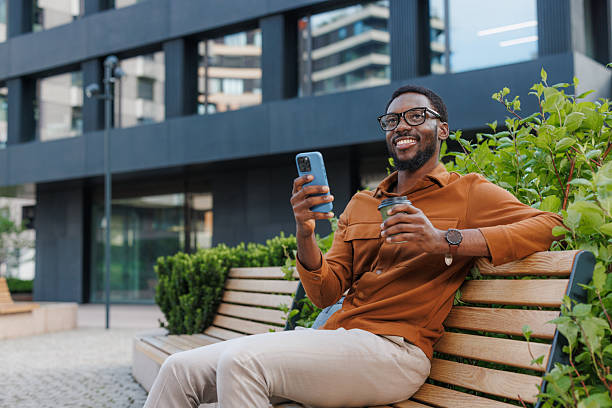 istock Smiling man relaxing on a park bench using his smartphone on a sunny day 2211257259
