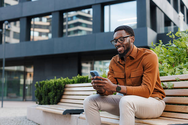 istock Man sitting on a bench smiling while using his smartphone outdoors 2211257282