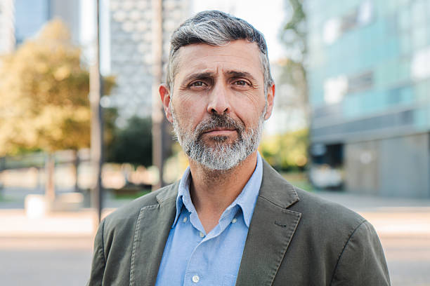 istock Confident mature businessman looking at camera with a serious expression, professional man with beard in a suit jacket standing outdoors in an urban setting, exuding leadership and experience 2211258377