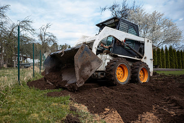 istock Skid Steer Loader Moving Soil Near Trees and Shrubs 2211258456