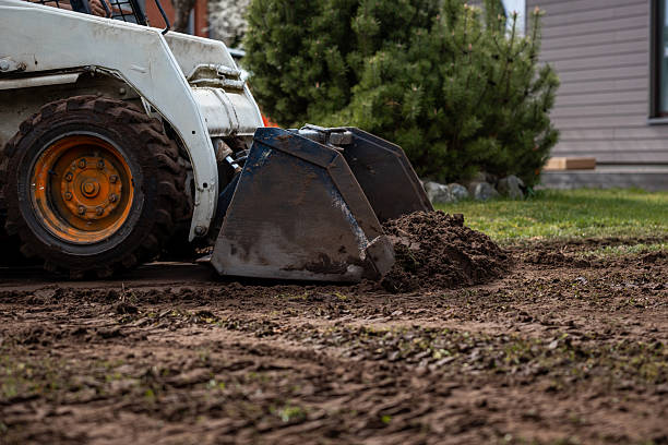 istock Skid Steer Loader Moving Soil Near Green Bush and Building 2211258490