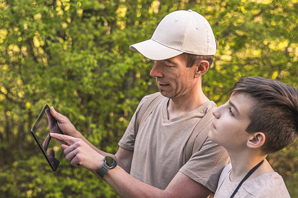 istock Birding. Father and son observing birds using binoculars and learning about them on digital tablet. Family time at weekend searching for birds or birdwatching in forest in late afternoon. 2211259400