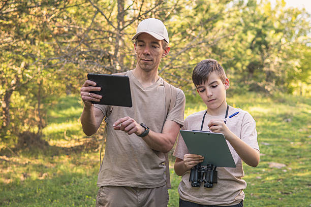 istock Birding. Father and son observing birds using binoculars and learning about them on digital tablet. Family time at weekend searching for birds or birdwatching in forest in late afternoon. 2211259425