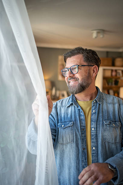 istock Smiling bearded man opening curtains at home 2211259620