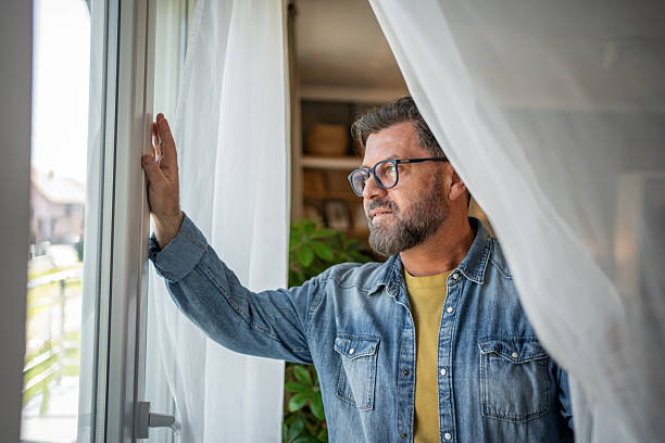 istock Pensive mature man looking out the window at home 2211259681