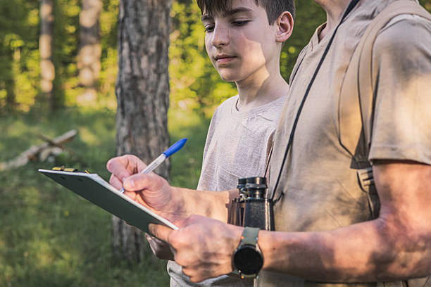 istock Birding. Father and son observing birds using binoculars and learning about them on digital tablet. Family time at weekend searching for birds or birdwatching in forest in late afternoon. 2211259737