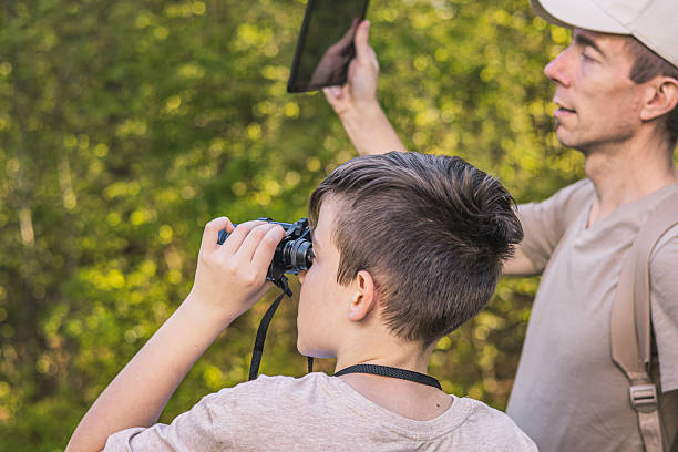 istock Birding. Father and son observing birds using binoculars and learning about them on digital tablet. Family time at weekend searching for birds or birdwatching in forest in late afternoon. 2211259834