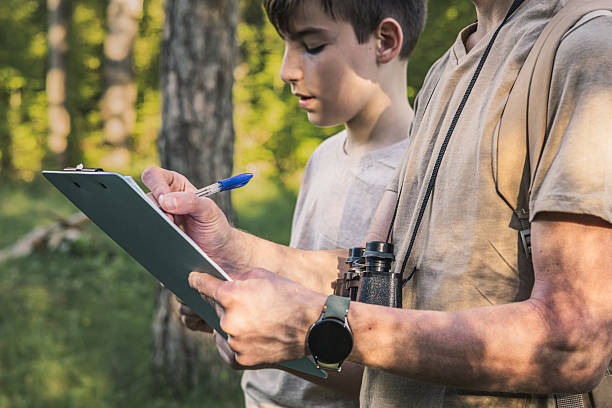 istock Birding. Father and son observing birds using binoculars and learning about them on digital tablet. Family time at weekend searching for birds or birdwatching in forest in late afternoon. 2211259896