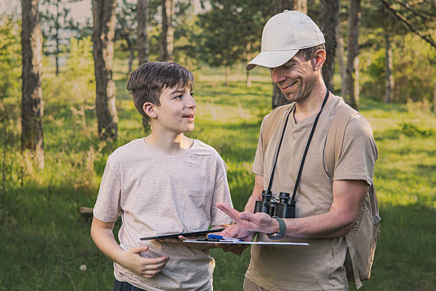 istock Birding. Father and son observing birds using binoculars, learning about them on digital tablet and feeding birds with birdseed. Family time at weekend searching for birds or birdwatching in forest in late afternoon. 2211259994