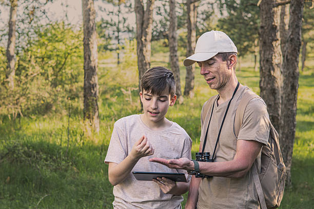 istock Birding. Father and son observing birds using binoculars, learning about them on digital tablet and feeding birds with birdseed. Family time at weekend searching for birds or birdwatching in forest in late afternoon. 2211260263
