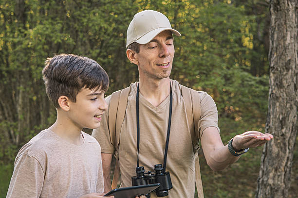 istock Birding. Father and son observing birds using binoculars, learning about them on digital tablet and feeding birds with birdseed. Family time at weekend searching for birds or birdwatching in forest in late afternoon. 2211260361