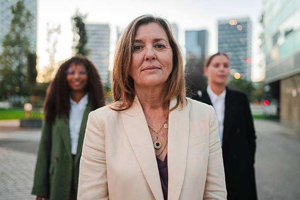 istock Confident female leader standing outdoors with colleagues in the background, symbolizing teamwork, leadership, and professional successat the job. Mature businesswoman looking at camera 2211260377