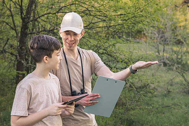 istock Birding. Father and son observing birds using binoculars, learning about them on digital tablet and feeding birds with birdseed. Family time at weekend searching for birds or birdwatching in forest in late afternoon. 2211260514