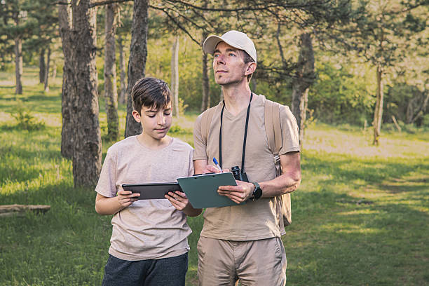 istock Birding. Father and son observing birds using binoculars and learning about them on digital tablet. Family time at weekend searching for birds or birdwatching in forest in late afternoon. 2211260866