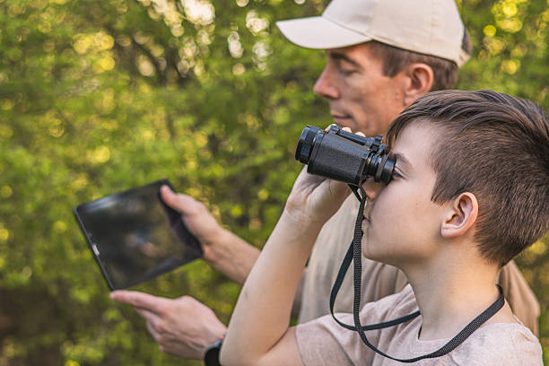 istock Birding. Father and son observing birds using binoculars and learning about them on digital tablet. Family time at weekend searching for birds or birdwatching in forest in late afternoon. 2211260925