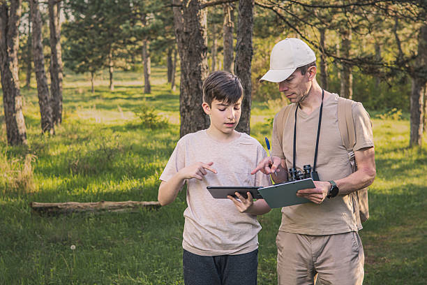 istock Birding. Father and son observing birds using binoculars and learning about them on digital tablet. Family time at weekend searching for birds or birdwatching in forest in late afternoon. 2211261048