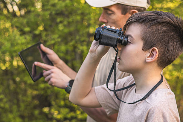istock Birding. Father and son observing birds using binoculars and learning about them on digital tablet. Family time at weekend searching for birds or birdwatching in forest in late afternoon. 2211261277