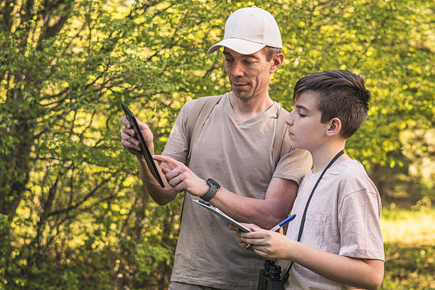 istock Birding. Father and son observing birds using binoculars and learning about them on digital tablet. Family time at weekend searching for birds or birdwatching in forest in late afternoon. 2211261326