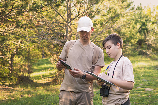 istock Birding. Father and son observing birds using binoculars and learning about them on digital tablet. Family time at weekend searching for birds or birdwatching in forest in late afternoon. 2211261443