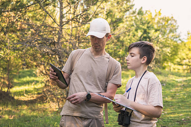istock Birding. Father and son observing birds using binoculars and learning about them on digital tablet. Family time at weekend searching for birds or birdwatching in forest in late afternoon. 2211261478