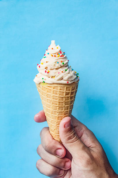 istock hand holding vanilla ice cream cone with sprinkles isolated on blue background 2211263550
