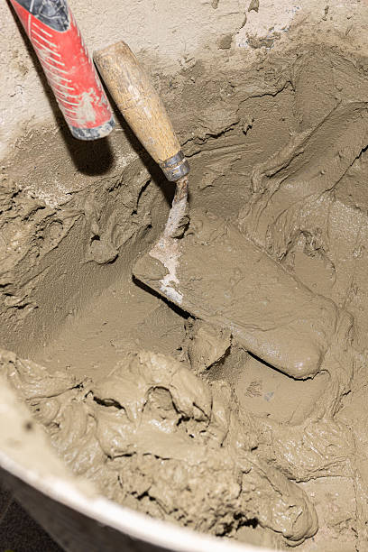 istock Construction worker preparing mortar for bricklaying, using a trowel and bucket on a building site 2211265741