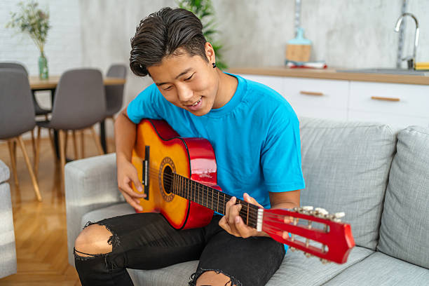 istock Young man playing acoustic guitar at home on sofa 2211268214
