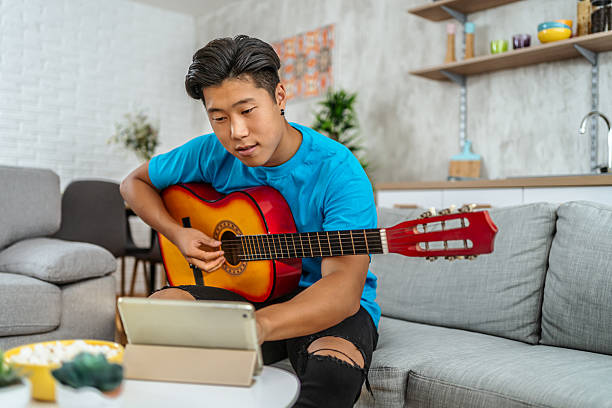 istock Young man learning to play guitar with online lessons at home 2211268248