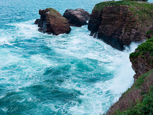 Dramatic ocean waves crashing against rocky cliffs with turquoise waters.