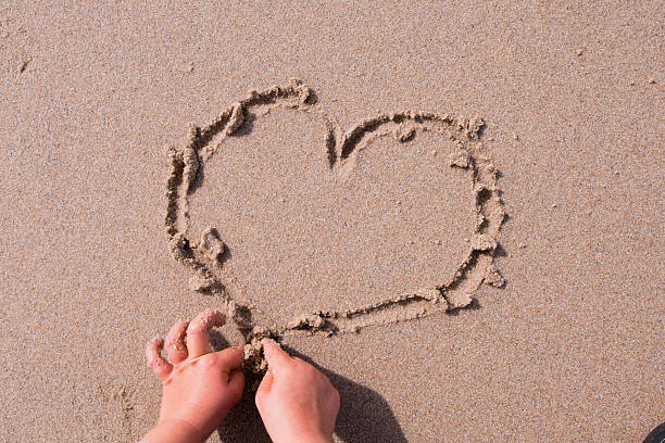 istock Child hands drawing heart shape on beach sand 2211269582