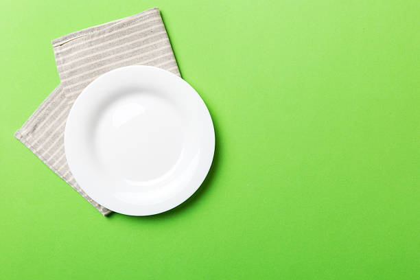 istock Top view on colored background empty round white plate on tablecloth for food. Empty dish on napkin with space for your design 2211271073