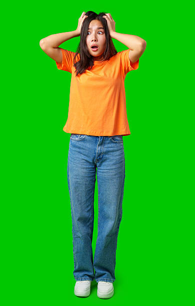 istock Surprised woman expressing shock while standing on a bright green background in a casual outfit 2211273504