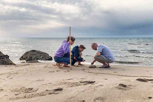istock Father explains barnacles on a stone to his kids at the beach 2211280361