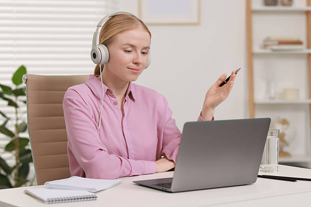 istock Interpreter in headphones having video chat via laptop at table indoors 2211281676