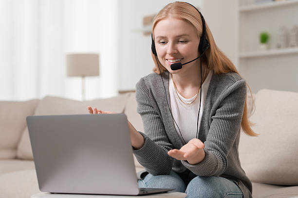 istock Interpreter in headset having video chat via laptop on sofa at home 2211281679