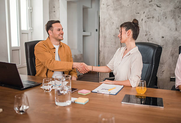 istock Two smiling business colleagues sitting at a conference table and shaking hands during a meeting with colleagues in a conference room, after a successful cooperation agreement 2211282238